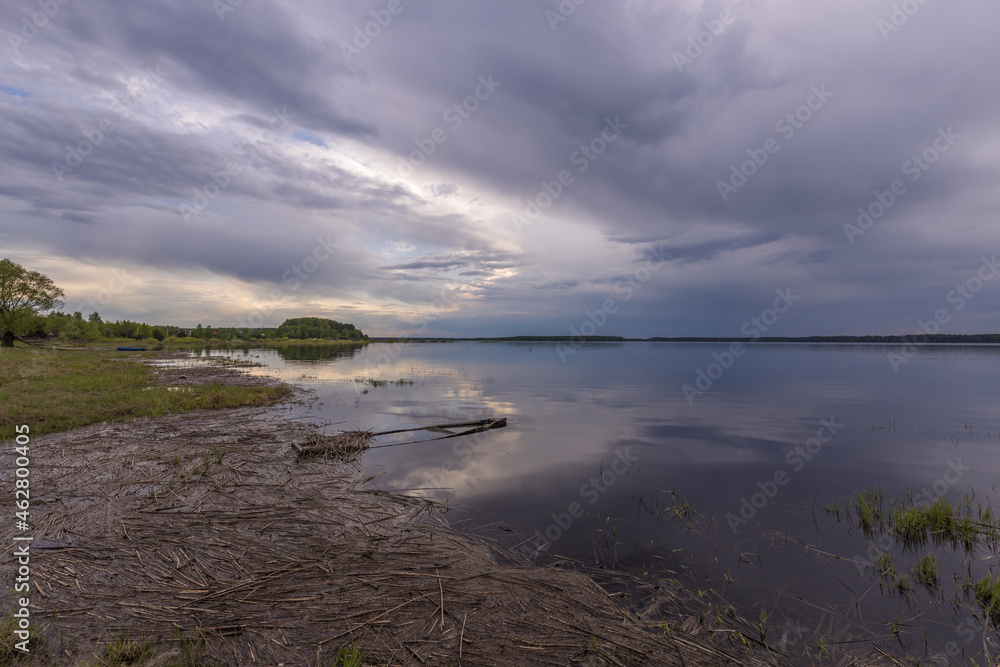 Evening landscape on the lake in early spring. The dramatic sky is reflected in the water.