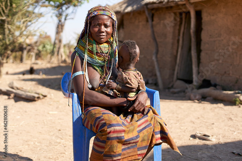Muhila traditional woman sitting on a blue chair, with baby on her lap, Congolo, Angola. photo