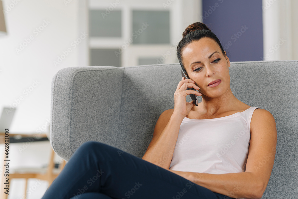 Businesswoman talking over smart phone while relaxing on sofa at home Businesswoman talking over smart phone while relaxing on sofa at home