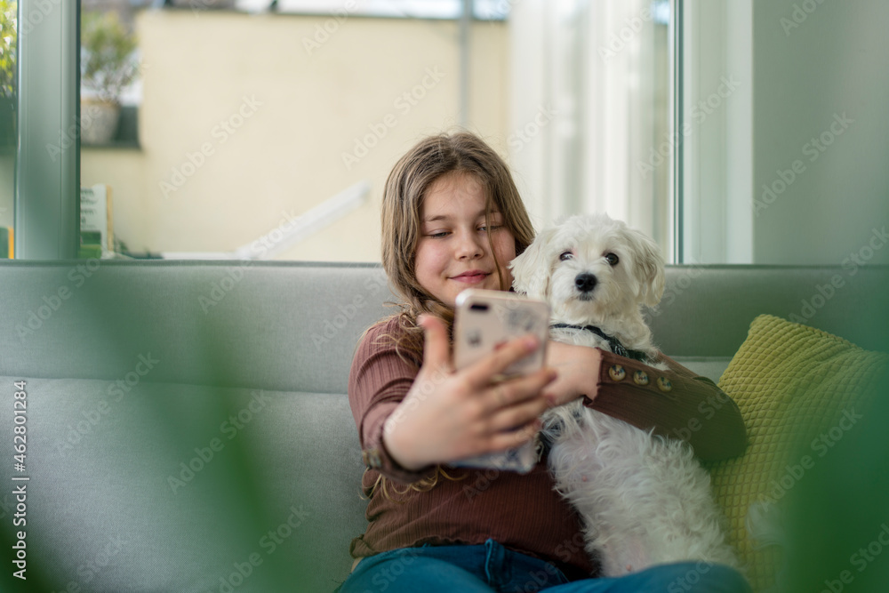 Girl taking selfie through smart phone with dog on sofa Girl taking selfie through smart phone with dog on sofa