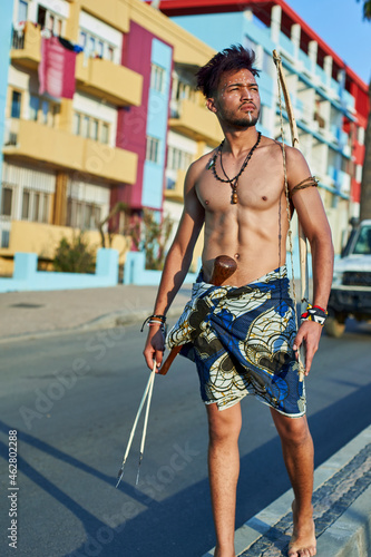 Tribal man with his traditional arch and arrows in the middle of the city with cars passing by, Lubango, Angola photo