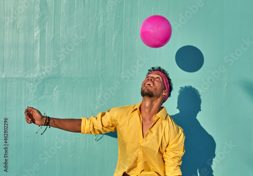 Young black man playing with a pink ball in front of a blue wall