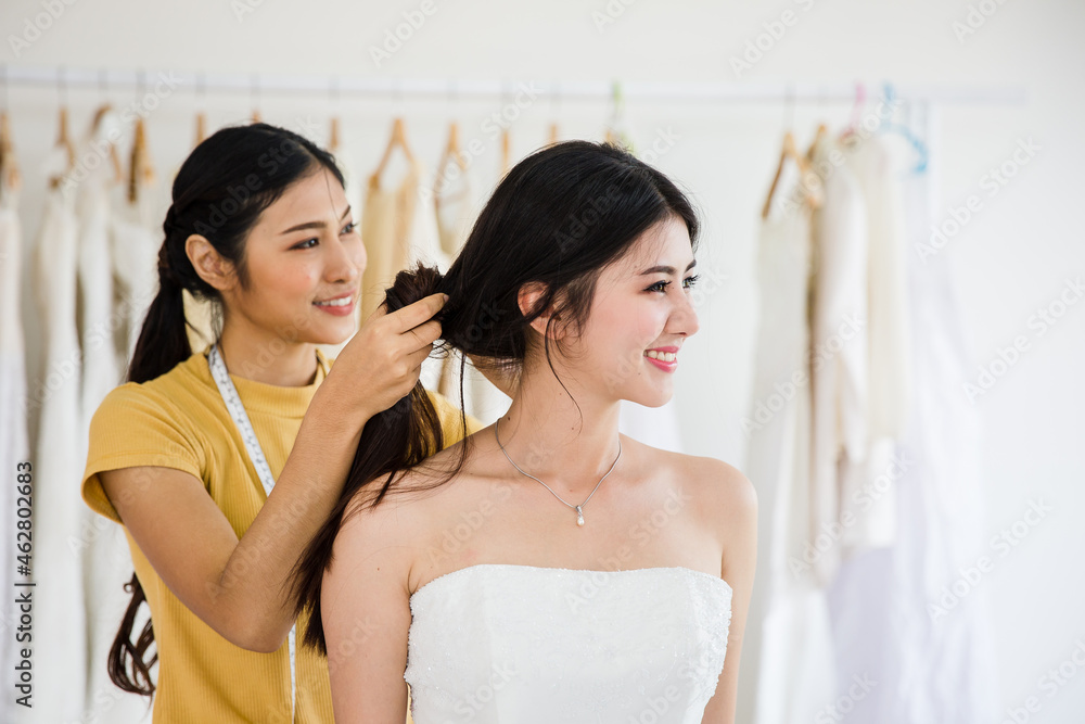 Attractive asian young bride is smiling in wedding dress with women assistant in wedding salon. Attractive asian young bride is smiling in wedding dress with women assistant in wedding salon.