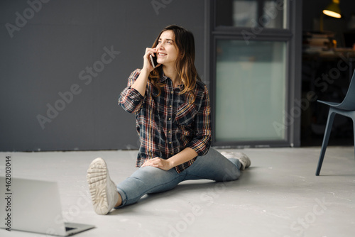 Smiling freelancer on the phone doing the splits on floor of a loft looking at distance photo