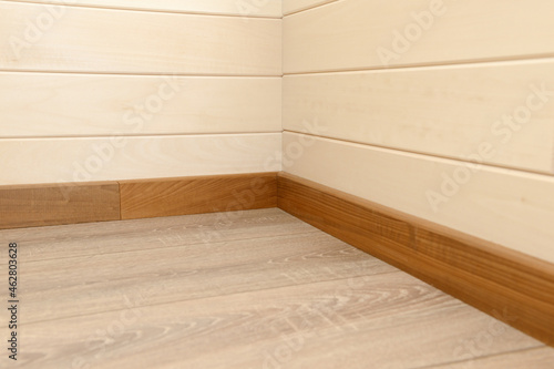 Corner of the house covered with wooden panels, wooden skirting board and wooden floor