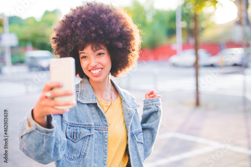 Happy young woman with afro hairdo taking a selfie in the city