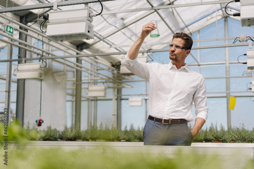 Male scientist holding conical flask while standing in greenhouse Male scientist holding conical flask while standing in greenhouse