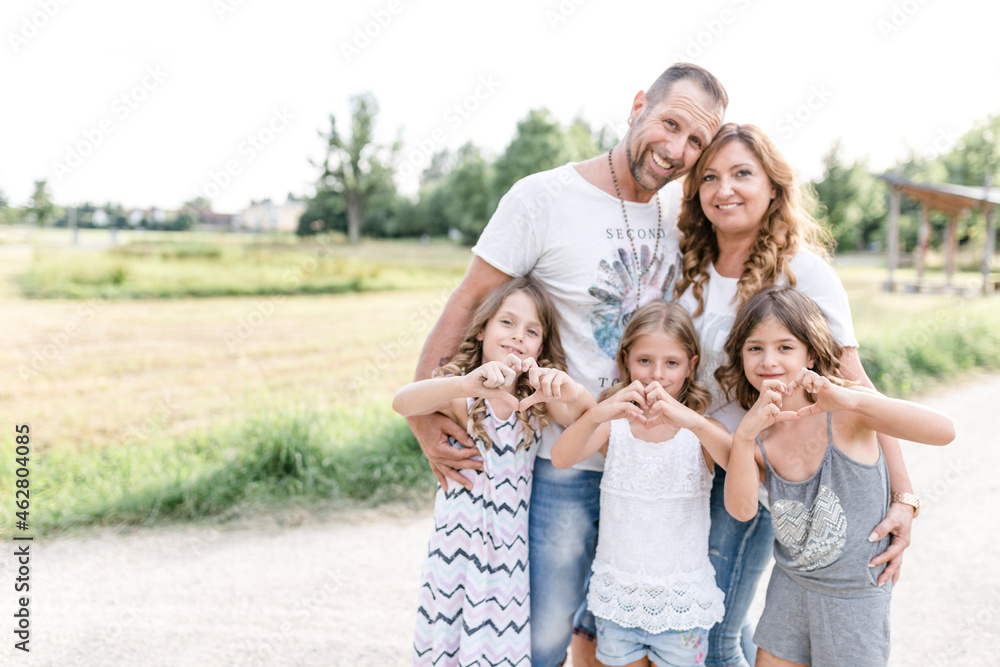 Happy parents with three triplet sisters shaping a heart outdoors Happy parents with three triplet sisters shaping a heart outdoors