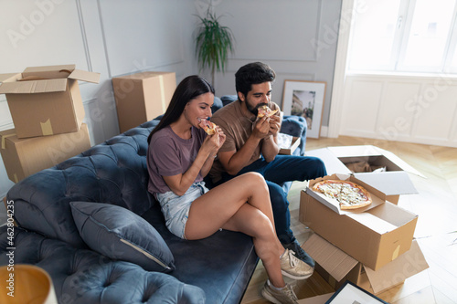 Young couple enjoying in pizza for lunch at new apartment.