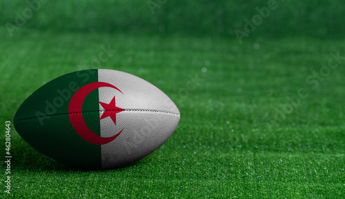 American football ball with Algeria flag on green grass background, close up