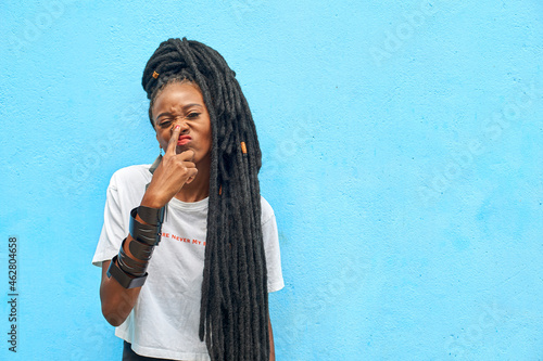 Portrait of woman with long dreadlocks touching her nose in front of turquoise wall photo