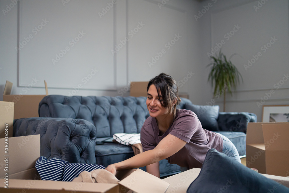 Obraz premium Smiling woman unpacking her belongings after moving into new home.