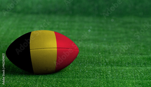 American football ball with Belgium flag on green grass background, close up