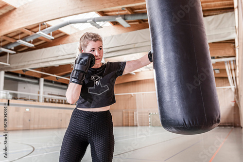 Female boxer practising at punchbag in sports hall photo