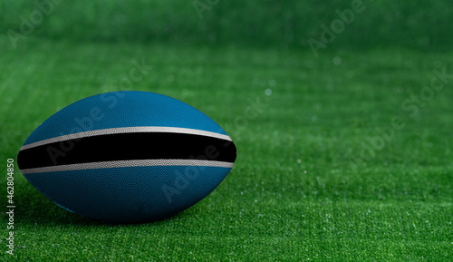 American football ball with Botswana flag on green grass background, close up