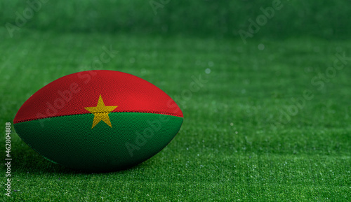 American football ball  with Burkina Faso flag on green grass background  close up