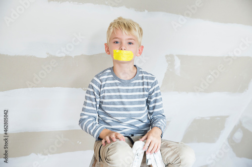Portrait of boy with taped mouth sitting on ladder in attic to be renovated
