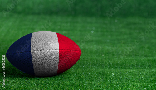 American football ball with France flag on green grass background, close up