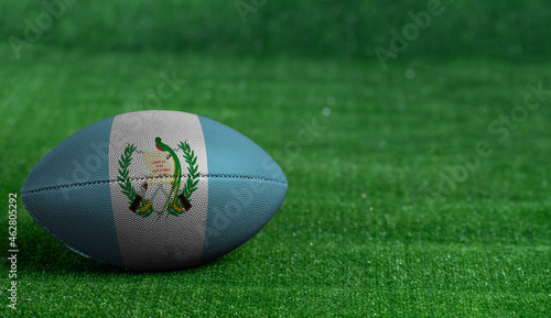 American football ball with Guatemala flag on green grass background, close up