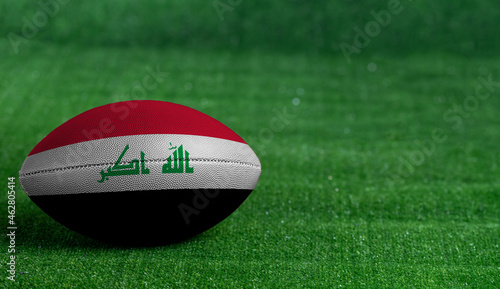 American football ball with Iraq flag on green grass background, close up