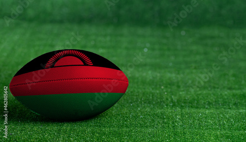 American football ball with Malawi flag on green grass background, close up