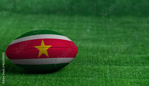 American football ball with Suriname flag on green grass background, close up