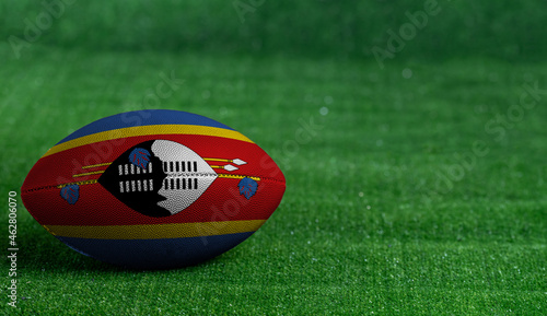 American football ball with Swaziland flag on green grass background, close up