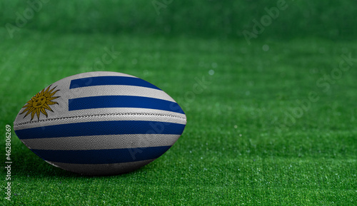 American football ball with Uruguay flag on green grass background, close up