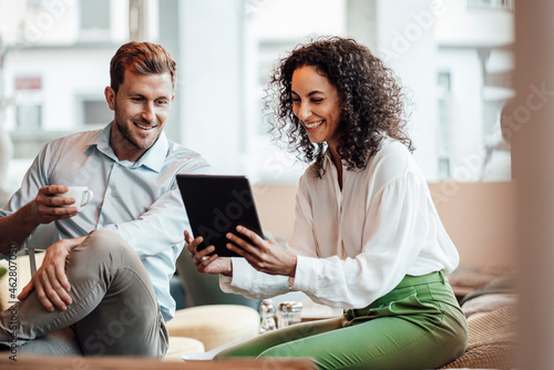 Smiling businesswoman using digital tablet while sitting with colleague at cafe photo