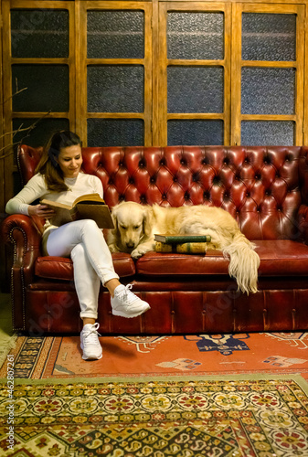 Woman with dog sitting on couch in a vintage shop reading an old book photo