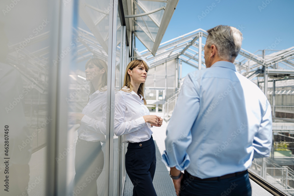 Business professionals discussing while standing by wall at greenhouse Business professionals discussing while standing by wall at greenhouse