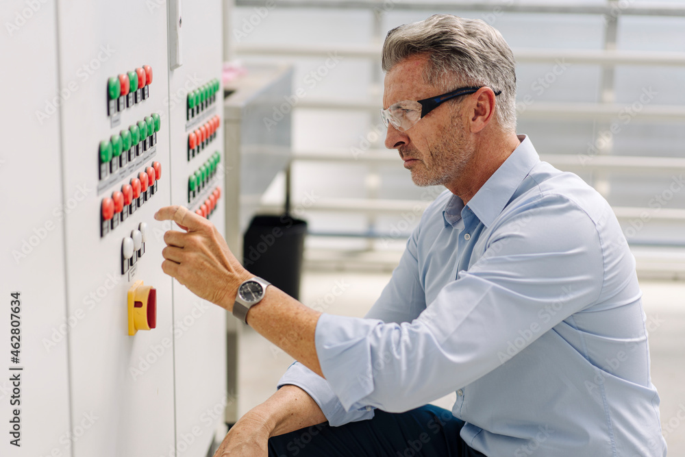 Businessman operating control panel while crouching in greenhouse Businessman operating control panel while crouching in greenhouse