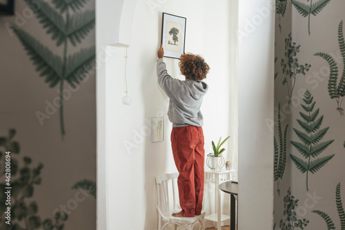 Young woman hanging up picture at home
