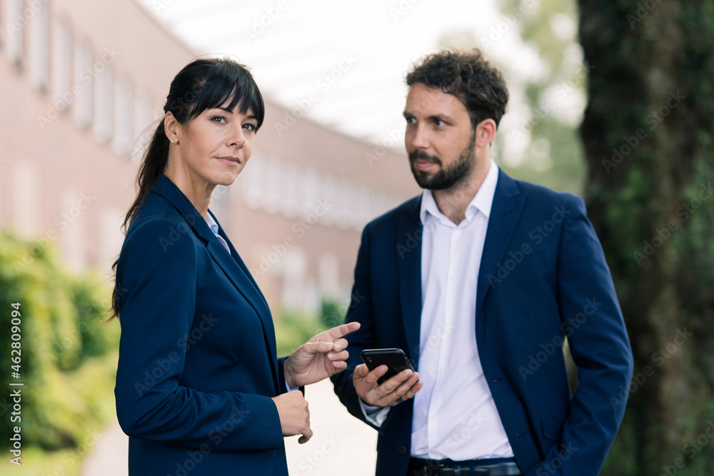 Confident businesswoman standing by male colleague holding smart phone Confident businesswoman standing by male colleague holding smart phone