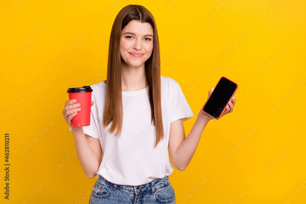 Photo of positive young happy woman smile show phone screen empty space hold coffee isolated on yellow color background - obrazy, fototapety, plakaty 