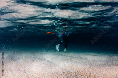 Underwater view of legs of man walking on sandy sea bottom photo
