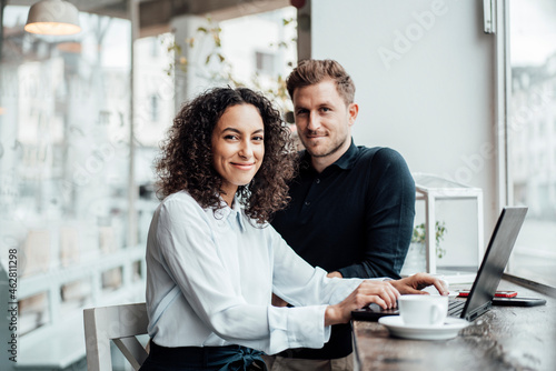 Confident businesswoman sitting by colleague with laptop at cafe photo