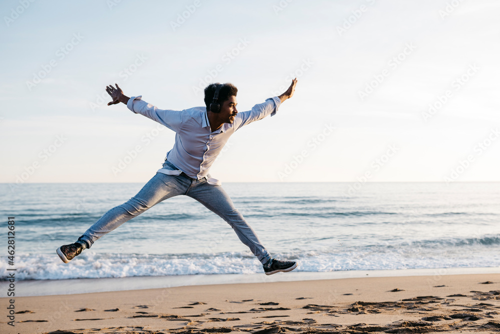 Cheerful man with arms outstretched jumping at beach against clear sky Cheerful man with arms outstretched jumping at beach against clear sky