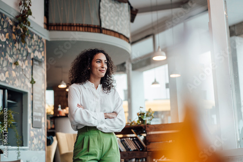 Thoughtful businesswoman looking away while standing with arms crossed at cafe photo