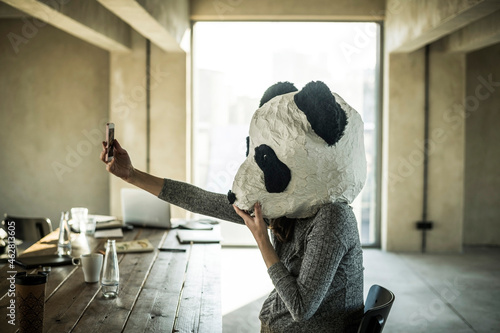 Woman with panda mask sitting in office, taking selfie photo