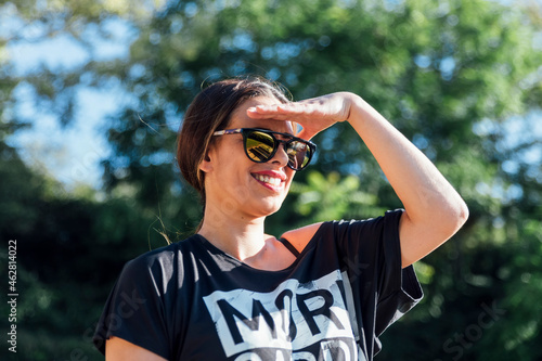 Close-up of beautiful woman wearing sunglasses shielding eyes against trees in park