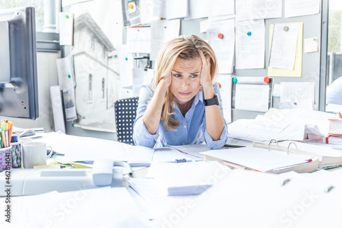 Despaired woman sitting at desk in office surrounded by paperwork photo