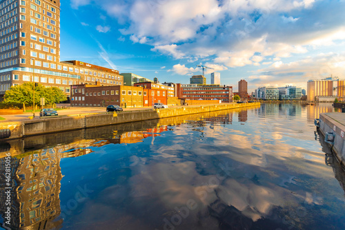 Buildings reflecting in canal by Oeresund in city against sky photo