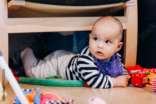 Cute little baby boy laying on the floor and watching aside. Many colorful toys around