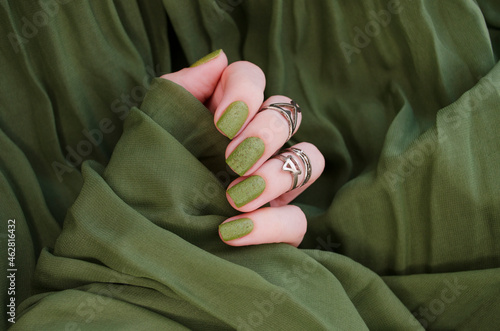 Closeup top view of beautiful painted in green nails isolated on green fabric background. Winter autumn nail style concept.