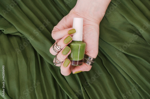 Closeup top view of beautiful painted in green nails isolated on green fabric background. Winter autumn nail style concept.