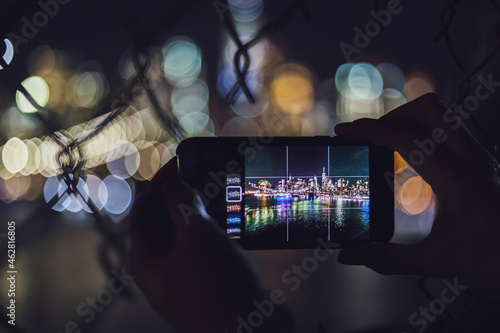 Close-up of woman taking smartphone picture of skyline at night, Manhattan, New York City, USA