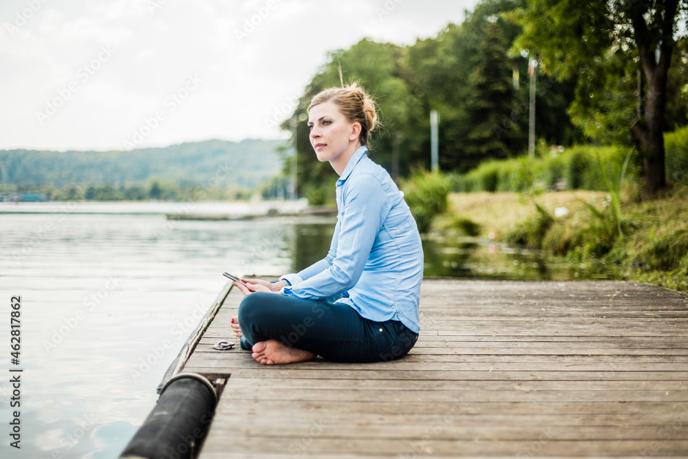 Woman sitting on jetty at a lake using tablet
