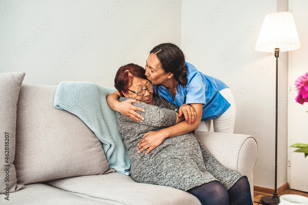 Senior Woman Sitting In Chair And Laughing With Nurse In Retirement Home. Professional helpful caregiver comforting smiling senior woman at nursing home