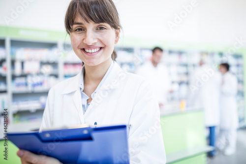 Portrait of smiling pharmacist in pharmacy holding clipboard photo